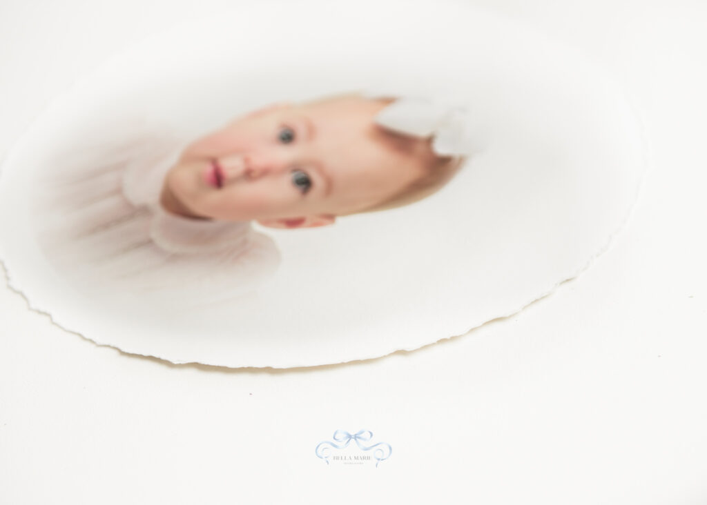 Image of a deckled print of a baby girl in a pale pink dress with Peter Pan collar and white bow in hair.   